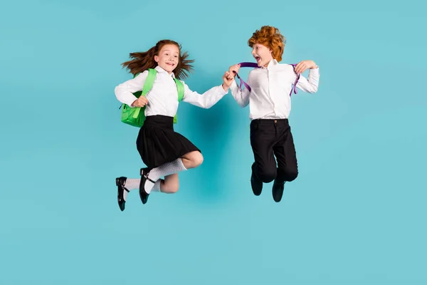 Фотографія стрибка двох школярів насолоджуйтесь польотом сумка біла сорочка уніформа ізольований синій колір фону — стокове фото