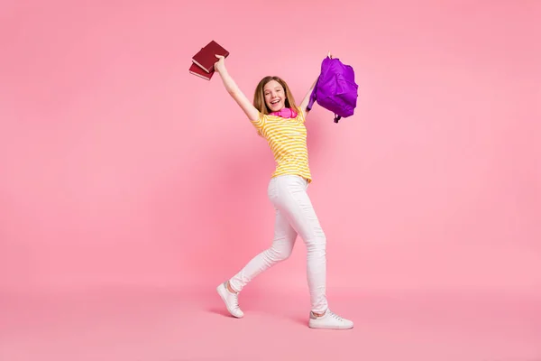 Φωτογραφία από αστεία χαλαρή κοπέλα σηκώστε τα χέρια τα πόδια μεταφέρουν τσάντα βιβλίο φορούν ριγέ κίτρινο t-shirt απομονωμένο ροζ χρώμα φόντο — Φωτογραφία Αρχείου