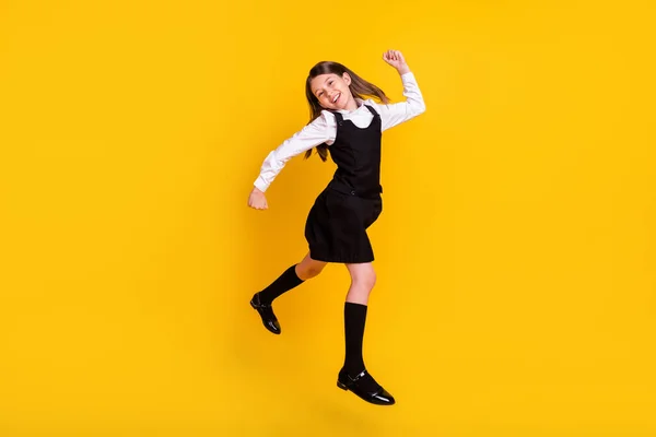 Фотография школьницы в форме в полный рост, прыгающей, как победитель, на ярко-желтом фоне — стоковое фото