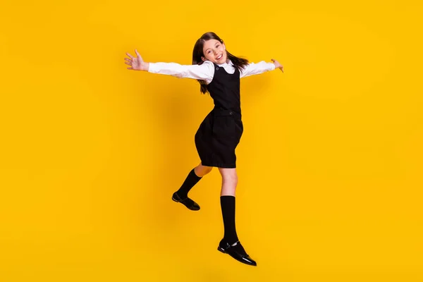 Фотография школьницы в форме в полный рост, прыгающей высоко, на ярко-желтом фоне — стоковое фото