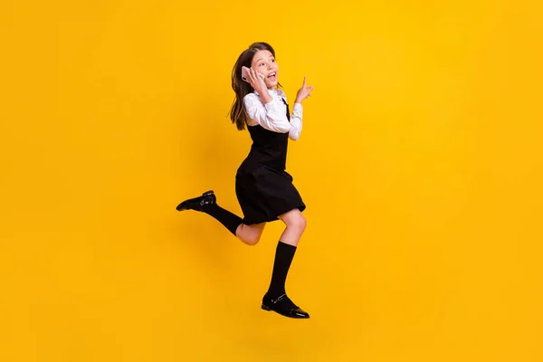 Full size foto van brunette klein meisje springen dragen uniform formalwear lange sokken praten telefoon lege ruimte geïsoleerd op gele kleur achtergrond — Stockfoto