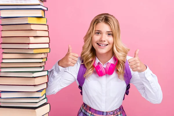 Retrato de atractiva chica de pelo ondulado alegre con un libro de pila que muestra el pulgar aislado sobre el fondo de color pastel rosa — Foto de Stock