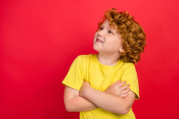 Foto de niño pequeño soñador creativo cruzó las manos mirada espacio vacío desgaste camiseta amarilla aislado fondo de color rojo — Foto de Stock