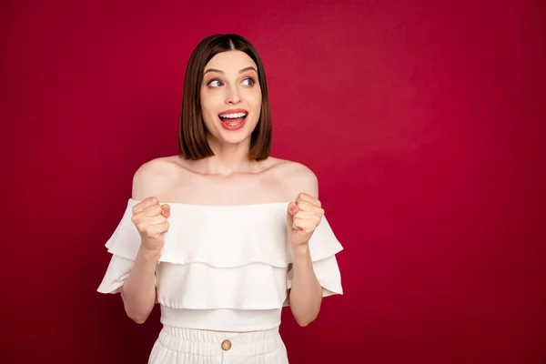 Photo of funky brown hairdo young lady hands fists look empty space wear white bare shoulders top isolated on red color background — Stock Photo, Image