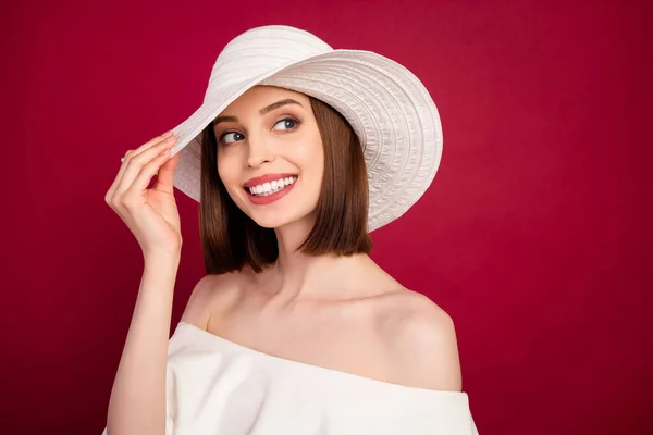 Foto de bonito penteado marrom jovem senhora olhar espaço vazio desgaste boné branco nua ombros blusa isolada no fundo vermelho — Fotografia de Stock