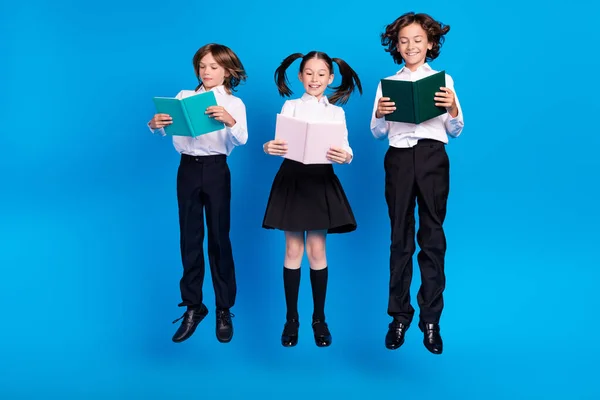 Foto de saltos escolares inteligentes leer interesante novela usar zapatos uniformes aislados color azul fondo —  Fotos de Stock