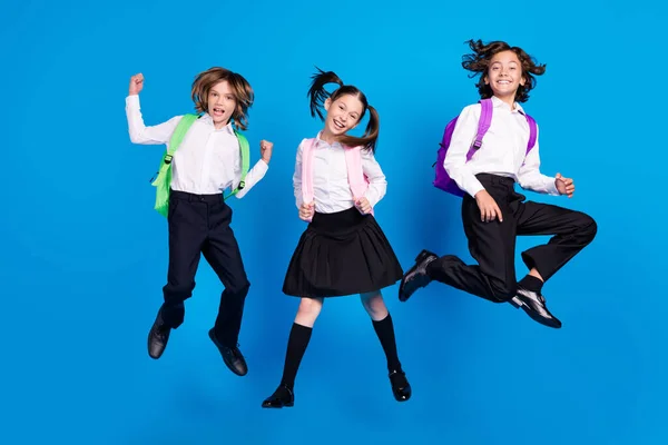 Фото божевільних розслаблених дітей стрибають хлопчик святкують перемогу в одязі рюкзак уніформа взуття ізольовані синій колір фону — стокове фото