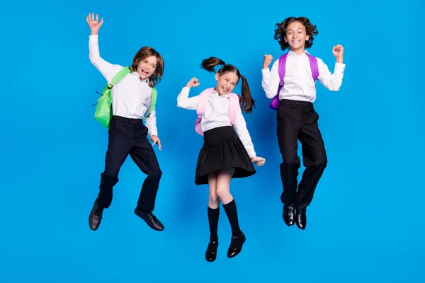 Foto de encantadoras mochilas formales escolares afortunados sonriendo saltando puños altos y ascendentes aislado color azul de fondo — Foto de Stock