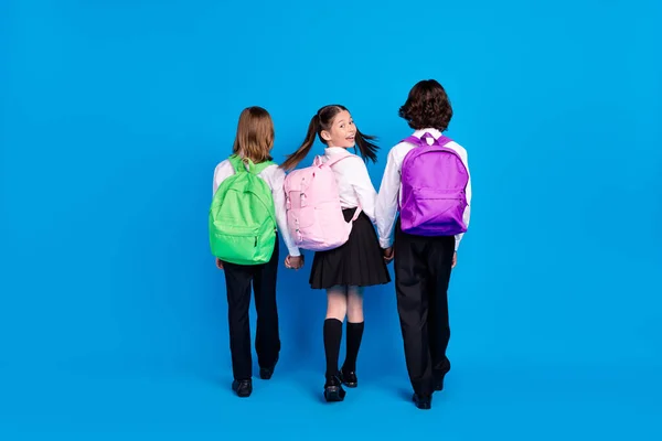 Foto de brilhante engraçado escola crianças formalwear mochilas sorrindo andando segurando braços isolado azul cor fundo — Fotografia de Stock