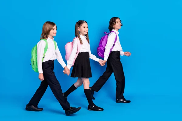 Foto van grappige charmante schoolkinderen dragen uniform rugzakken met armen lopen glimlachend geïsoleerde blauwe kleur achtergrond — Stockfoto