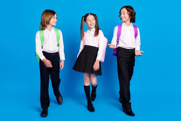 Foto de adorables escolares divertidos usan mochilas uniformes caminando sonriendo aislado fondo de color azul — Foto de Stock