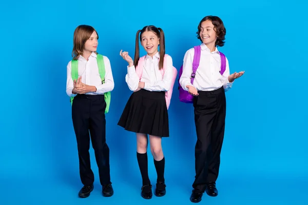 Foto de compañeros de clase positivos niños tienen conversación usan mochila uniforme aislado color azul fondo —  Fotos de Stock