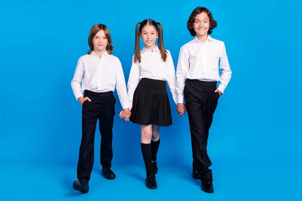 Фото солодких блискучих школярів носять уніформу, тримаючи руки, що йдуть, посміхаючись ізольований синій колір фону — стокове фото
