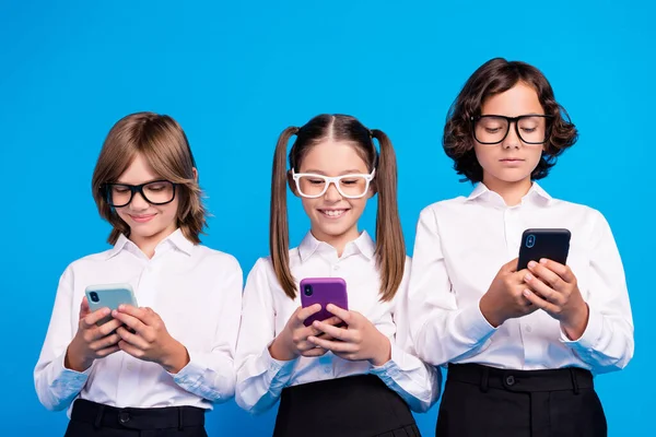 Foto de bloguero positivo escolares sostienen teléfono escribiendo SMS usar gafas uniforme aislado fondo de color azul —  Fotos de Stock