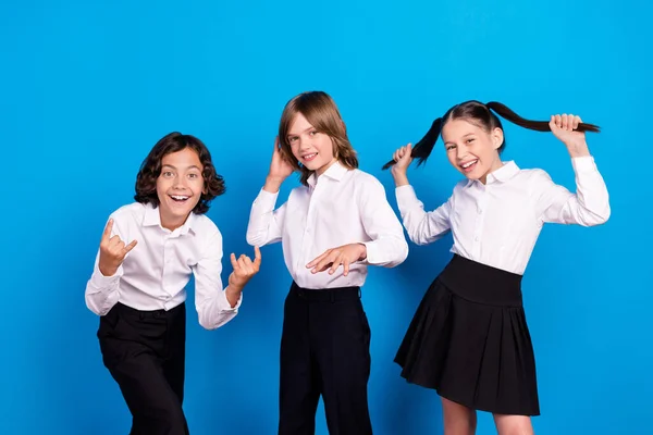 Foto de escolares despreocupados brillantes usan uniforme sonriente bailando mostrando el signo de roca aislado fondo de color azul — Foto de Stock