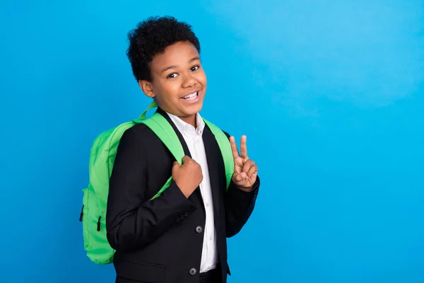 Foto de joven feliz alegre piel oscura niño sonrisa buen humor v-signo desgaste bolso aislado sobre fondo de color azul —  Fotos de Stock