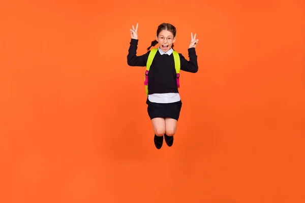 Foto de compañero de clase amigable funky salto mostrar dos v-signos de desgaste mochila uniforme aislado fondo de color naranja — Foto de Stock