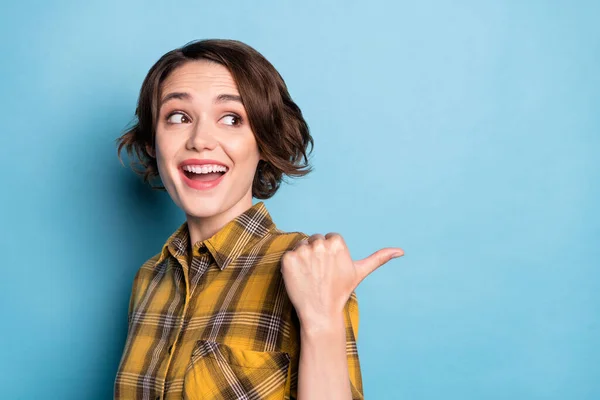 Foto de espantado curioso menina direto polegar de volta vazio espaço aberto boca desgaste xadrez camisa isolado azul cor fundo — Fotografia de Stock