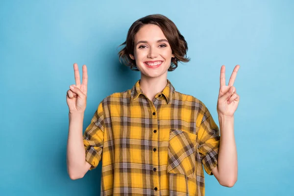 Foto de menina encantadora amigável mostrar dois v-sinais branco sorriso desgaste xadrez camisa isolado azul cor de fundo — Fotografia de Stock