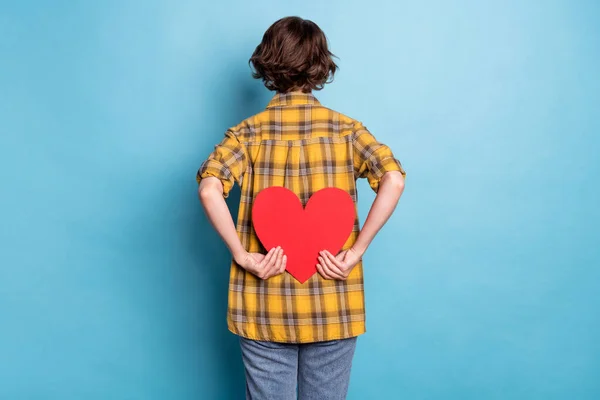 Фотографія заднього виду жінки тримає серце фігуру теперішнього одягу картатої сорочки ізольованого синього кольору фону — стокове фото