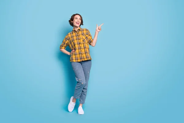 Foto de señora positiva dedo directo espacio vacío desgaste camisa a cuadros jeans zapatos aislados color azul fondo —  Fotos de Stock