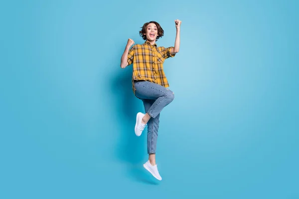 Foto de la señora alegre salto ganancia logro desgaste camisa a cuadros jeans zapatos aislados color azul fondo —  Fotos de Stock