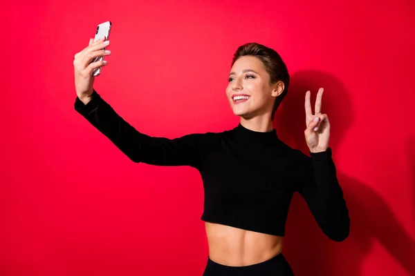 Portré vonzó trendi vidám lány blogger csinál szelfi bemutató v-jel elszigetelt felett élénk piros színű háttér — Stock Fotó