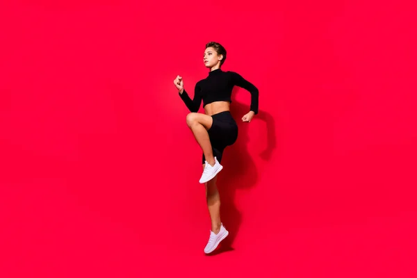 Foto de perfil de corredor dama seria jogging entrenamiento desgaste negro recortado superior aislado color rojo fondo — Foto de Stock