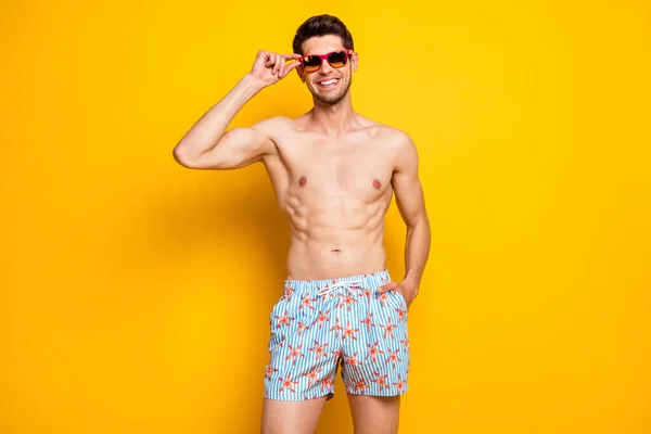 Портрет привабливого без сорочки веселого хлопця, який торкається специфікацій сезон морських курортів ізольований на яскраво-жовтому кольоровому фоні — стокове фото