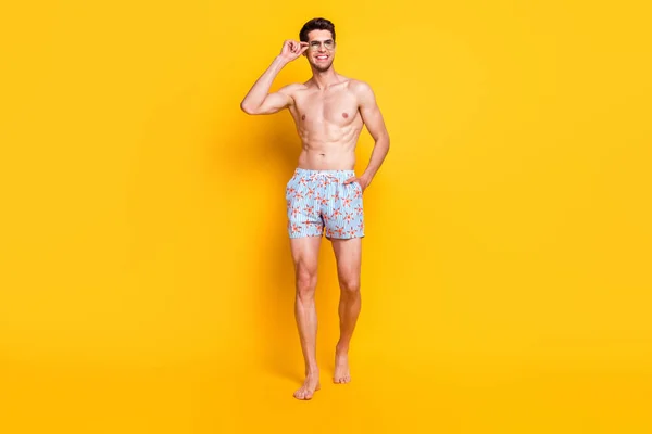 Foto de encantador lindo joven sin camisa vestido gafas oscuras sonriendo caminando aislado color amarillo fondo — Foto de Stock