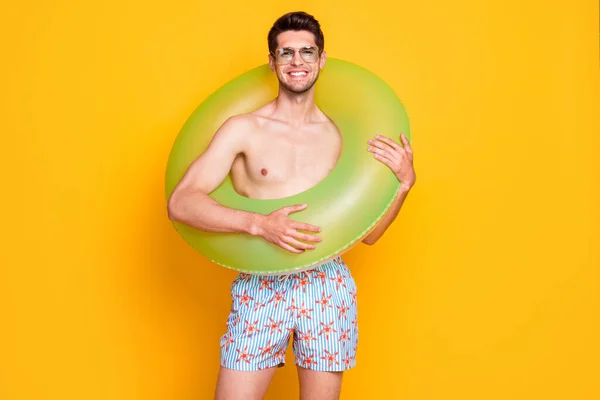 Foto de sexy divertido joven desnudo torso desgaste gafas oscuras caminando sosteniendo el círculo de agua sonriendo aislado color amarillo fondo — Foto de Stock