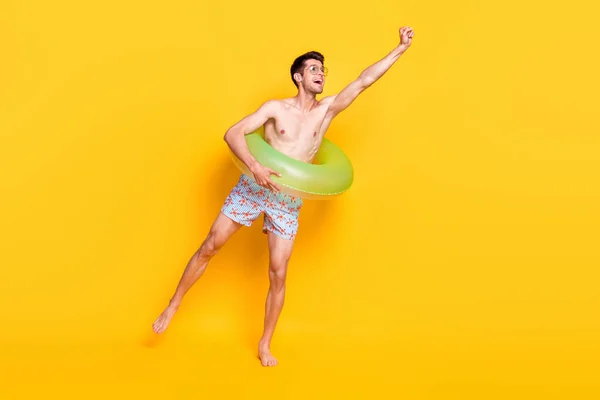 Foto de lindo tipo funky sin camisa vestido gafas oscuras sonriendo dentro boya captura brazo vacío espacio aislado color amarillo fondo — Foto de Stock