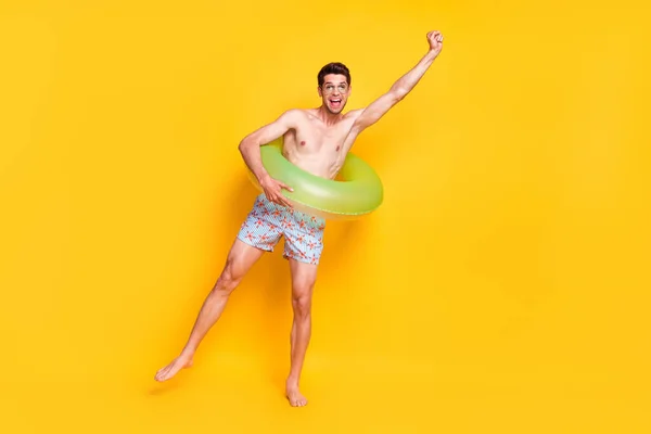 Full length body size view of attractive shirless wesoły facet having fun wearing life booy isolated over bright yellow color background — Zdjęcie stockowe