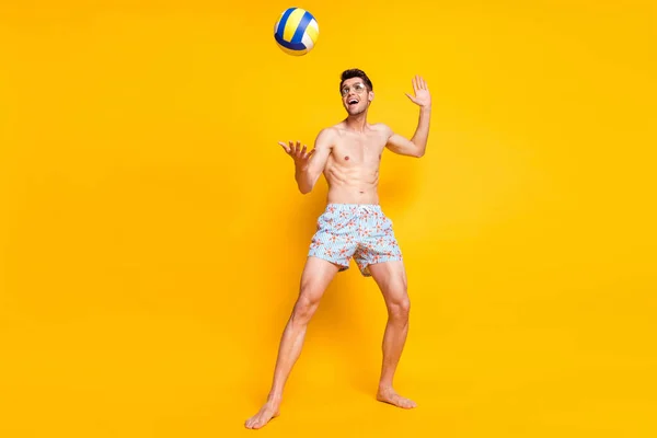 Foto von lustigen charmanten jungen Mann nackten Oberkörper tragen dunkle Brille spielen Volleyball lächeln isoliert gelbe Farbe Hintergrund — Stockfoto