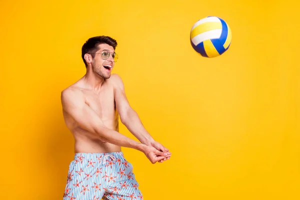 Foto de divertido bastante joven desnudo torso gafas oscuras jugando voleibol sonriendo aislado color amarillo fondo — Foto de Stock
