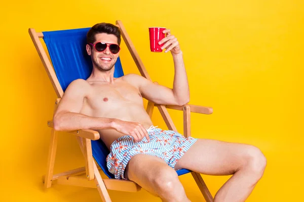 Photo de doux charismatique jeune homme nu torse allongé chaise longue boire de la bière isolé fond de couleur jaune — Photo