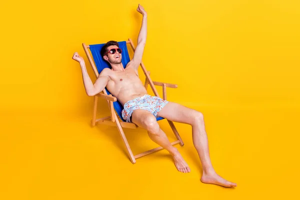 Foto di dolce divertente giovane ragazzo a torso nudo vestito occhiali scuri sdraiato poltrona allungamento isolato colore giallo sfondo — Foto Stock