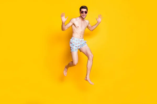 Φωτογραφία του χαρισματικού funky νεαρός άνδρας γυμνός κορμός φορούν σκούρα γυαλιά άλμα ψηλά χαμογελώντας απομονωμένο κίτρινο χρώμα φόντο — Φωτογραφία Αρχείου