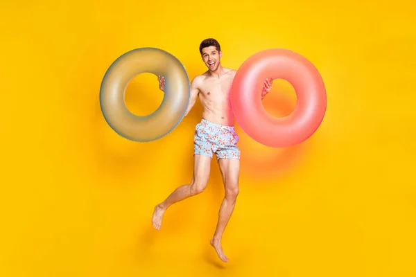 Photo pleine grandeur de jeune homme brunet impressionné sauter avec un short de port de bouée isolé sur fond jaune — Photo