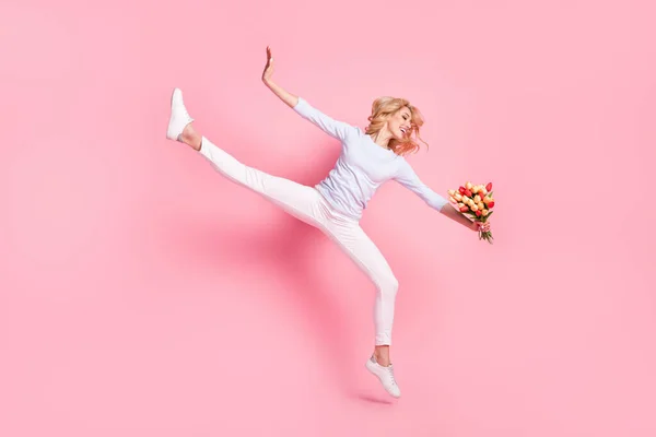 Полноразмерное фото счастливой симпатичной молодой женщины, подпрыгивающей вверх гибкими руками тюльпаны, изолированные на розовом цветовом фоне — стоковое фото