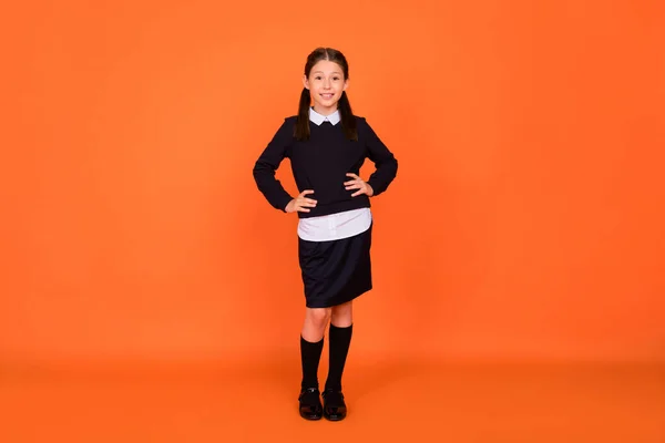 Photo of cheerful positive schoolgirl posing hands hips wear uniform isolated orange color background — Stock Photo, Image