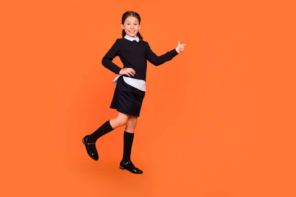 Vista completa del tamaño del cuerpo de la atractiva niña alegre preadolescente demostrando espacio de copia aislado sobre fondo de color naranja brillante — Foto de Stock