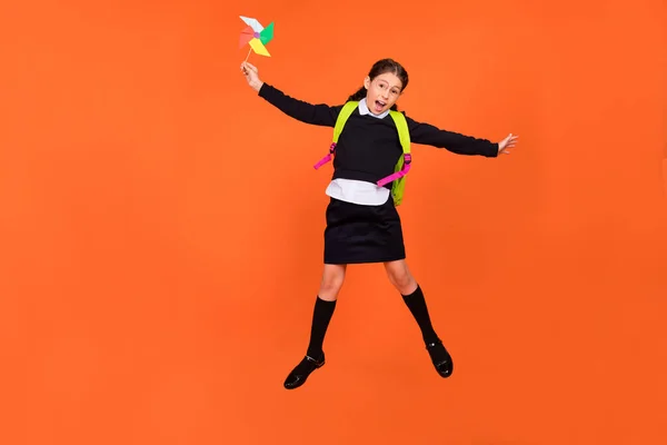 Photo of energetic schoolgirl jump hold propeller toy wear uniform rucksack isolated orange color background — Stock Photo, Image