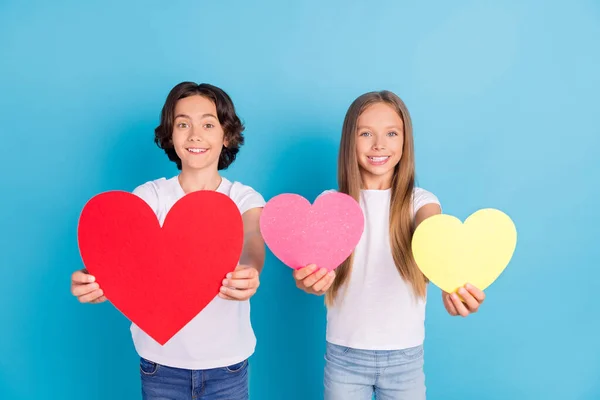 Foto de duas crianças afetuosas apresentando figuras do coração usar branco t-shirt isolado azul cor de fundo — Fotografia de Stock