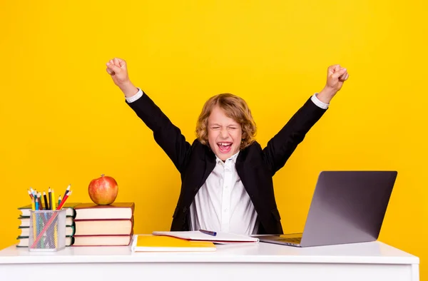 Foto van verbaasd kind zitten bureau schreeuwen vieren overwinning verhogen vuist dragen uniform geïsoleerde gele kleur achtergrond — Stockfoto