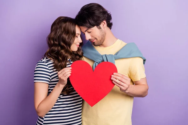 Foto von verträumt entzückenden Paar tragen lässige Kleidung lächelnd hält große Papierherz geschlossenen Augen isoliert violette Farbe Hintergrund — Stockfoto