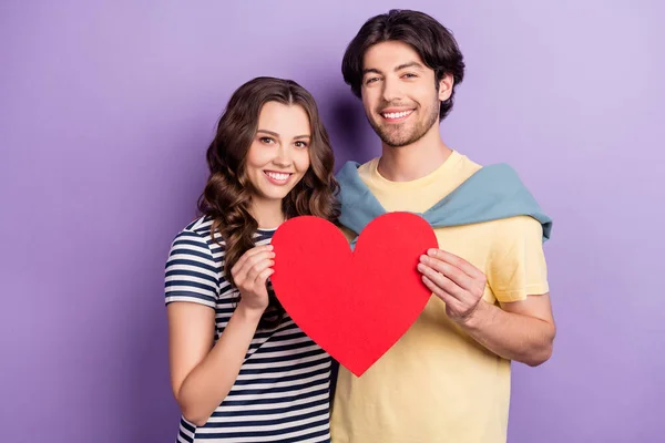 Photo of cute sweet lovers dressed casual outfit holding big red heart smiling isolated purple color background — Stock Photo, Image