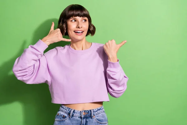 Portret van aantrekkelijke vrolijke meisje tonen bel me teken kopiëren ruimte geïsoleerd over helder groene kleur achtergrond — Stockfoto