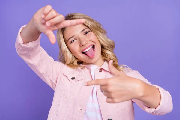 Portret van positieve zorgeloze tiener tong uit armen maken frame symbool geïsoleerd op violette kleur achtergrond — Stockfoto