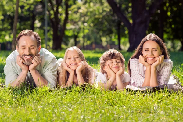 Retrato de familia alegre atractiva acostada en césped fresco pasar tiempo disfrutando de buen tiempo cálido día soleado al aire libre — Foto de Stock